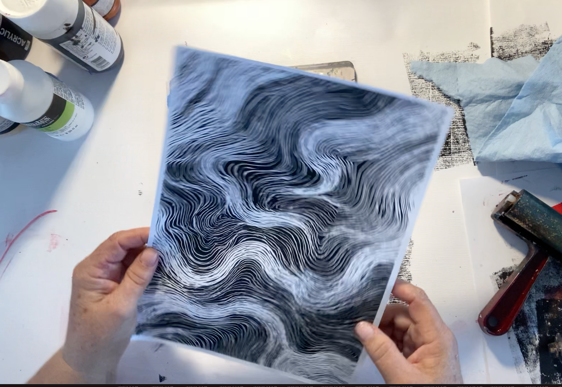 Artist holding a piece of paper with black and white abstract pattern on a workbench.